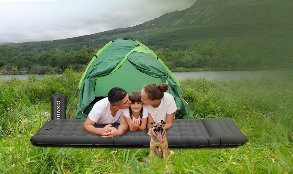 Inflatable camping sleeping mat with foot pump and pillow, blue and gray color, set up on grassy ground in outdoor environment